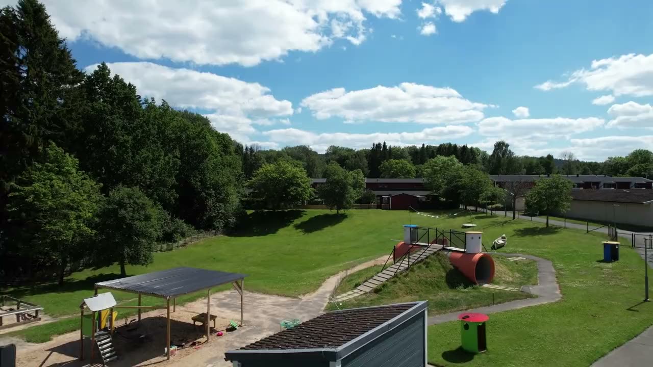 Delfinens gård från luften: den blå förskolebyggnaden, gräsbacken med rutschkanetunnlar inbyggda i sluttningen och skogen runt om.
