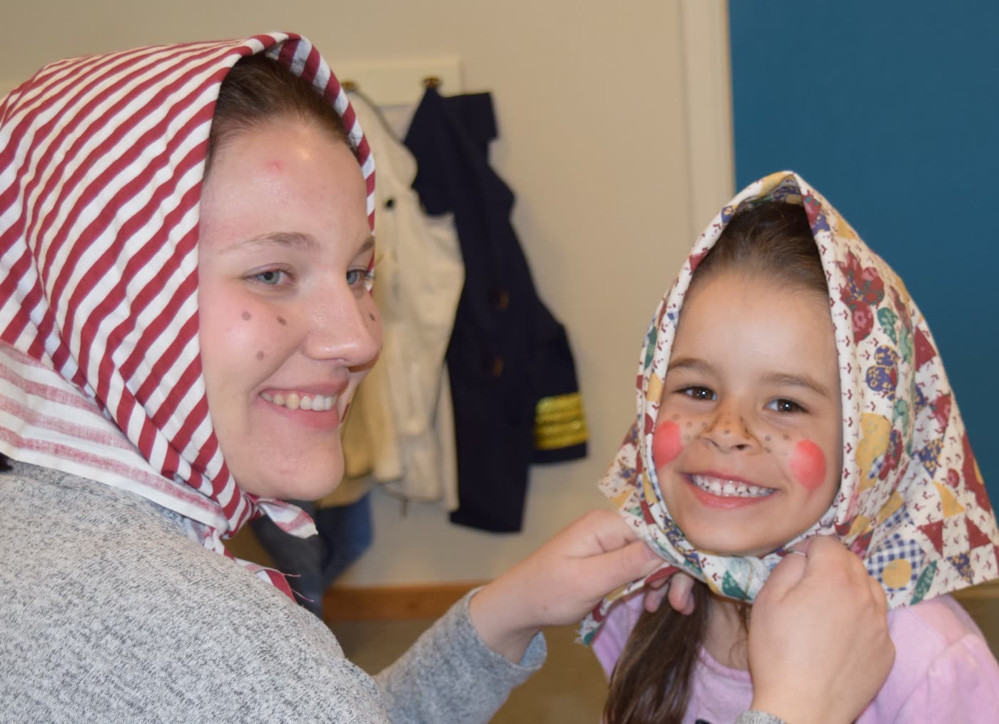 En pedagog och ett skrattande barn, båda med sjalett på huvudet, tittar på varandra inne i hallen.